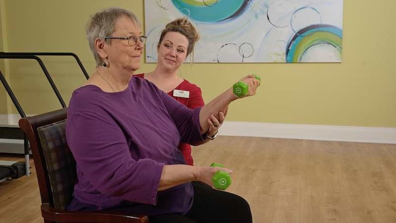 A senior woman lifts weights with the supervision of an on-site physical therapist at Allegro Richmond Heights