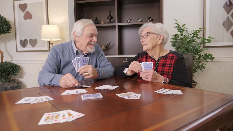 a senior couple playing cards together in a common area of the Richmond Heights community